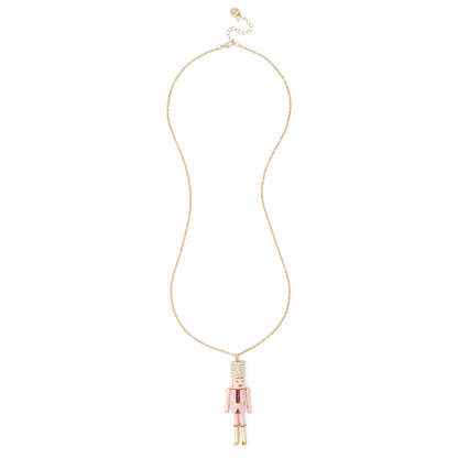 A delicate gold chain necklace featuring a small nutcracker pendant with pink and white enamel detailing, displayed against a solid white background.