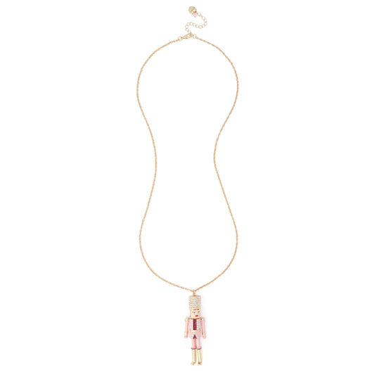 A delicate gold chain necklace featuring a small nutcracker pendant with pink and white enamel detailing, displayed against a solid white background.
