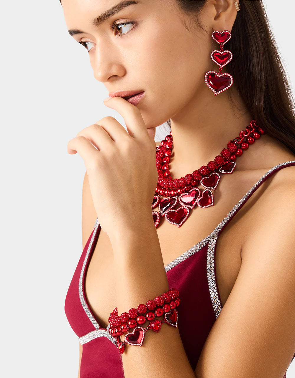 Woman wearing a red heart-themed jewelry set including necklace, earrings, and bracelet.