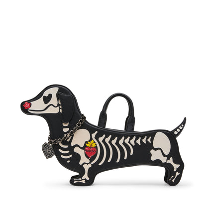 A black dachshund-shaped handbag with a skeleton design, featuring cream-colored bones, a red heart with a yellow flower on the spine, and a small red heart on the nose. It has a top handle, a shoulder strap, and a silver chain with a decorative tag, set against a plain white background.
