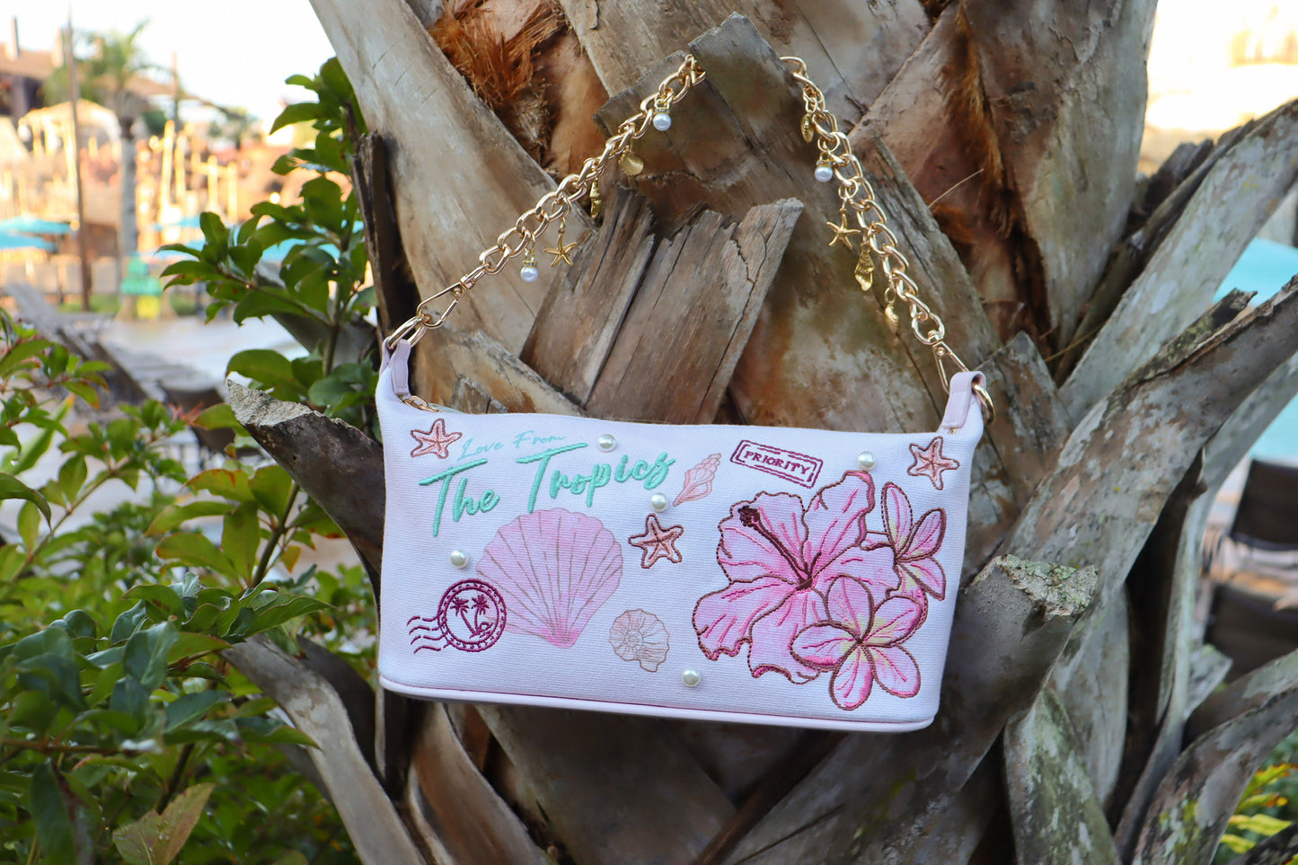 Handbag with tropical design and chain strap against a palm tree background