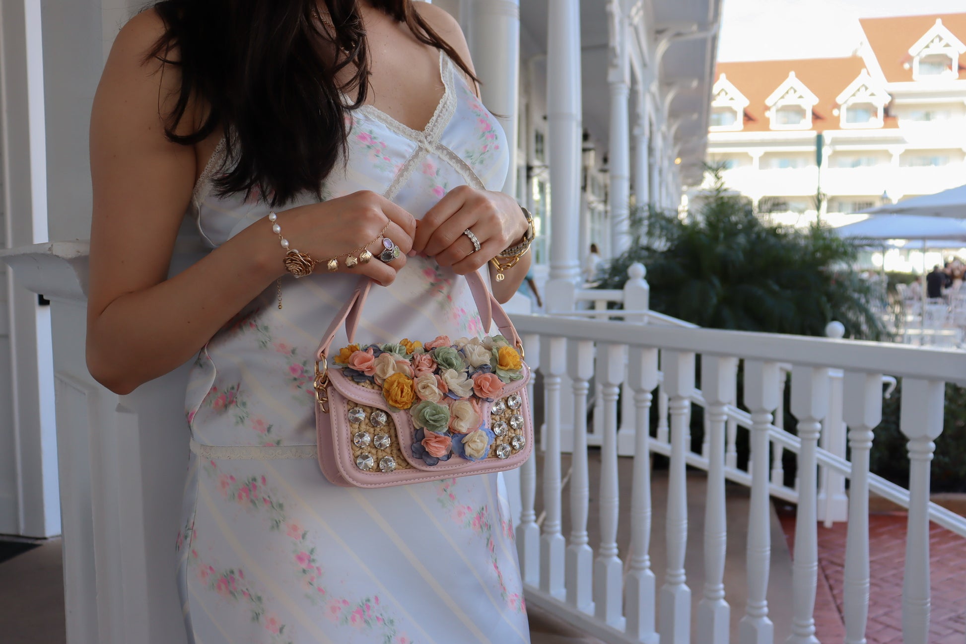 Woman holding a pink handbag with floral embellishments on a balcony.