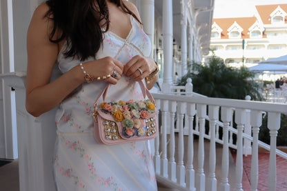 Woman holding a pink handbag with floral embellishments on a balcony.