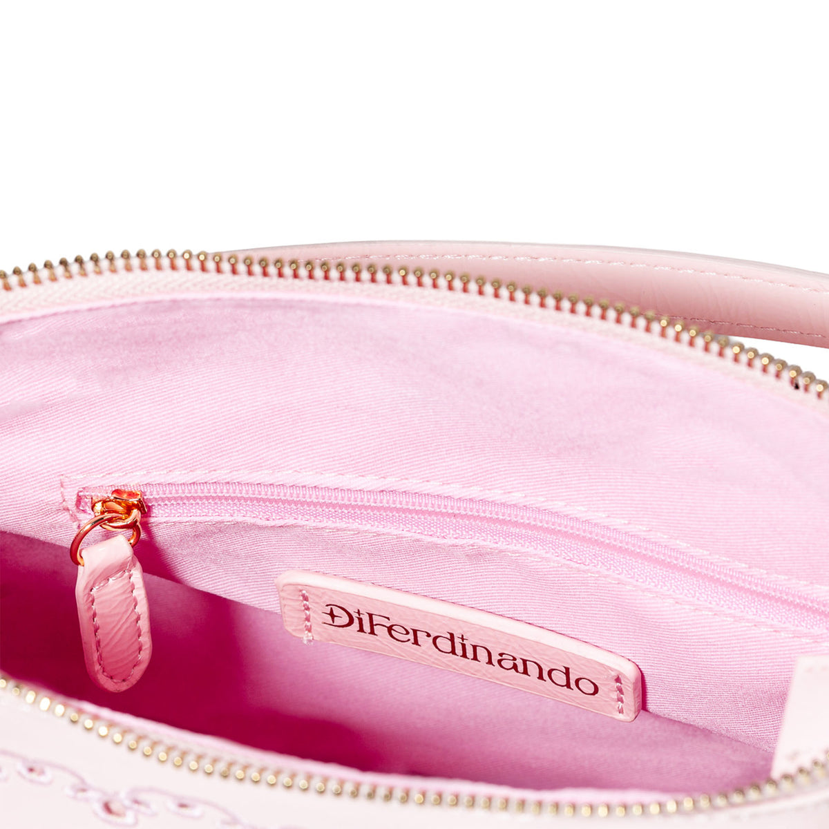Close-up of the interior of a light pink handbag or cosmetic pouch, showing a pink fabric lining, a top zipper with metallic teeth, a small zip pocket with a pink pull tab, and a sewn-in brand label reading DiFerdinando.