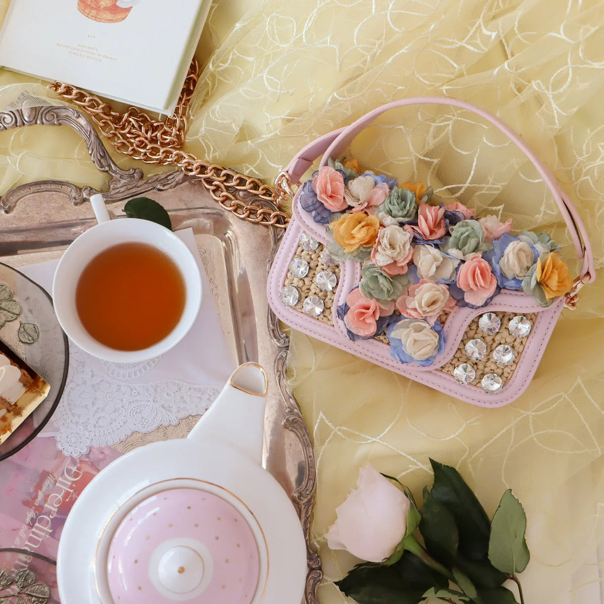 Decorative handbag with floral embellishments on a table with tea and pastries.