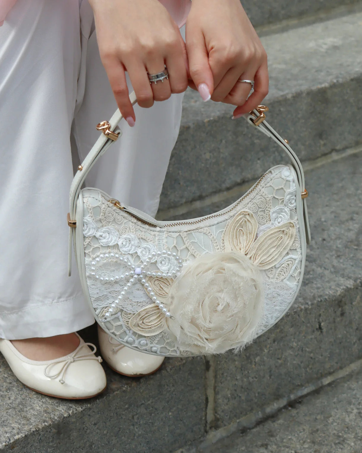 Person holding a decorative handbag with floral details on stone steps.