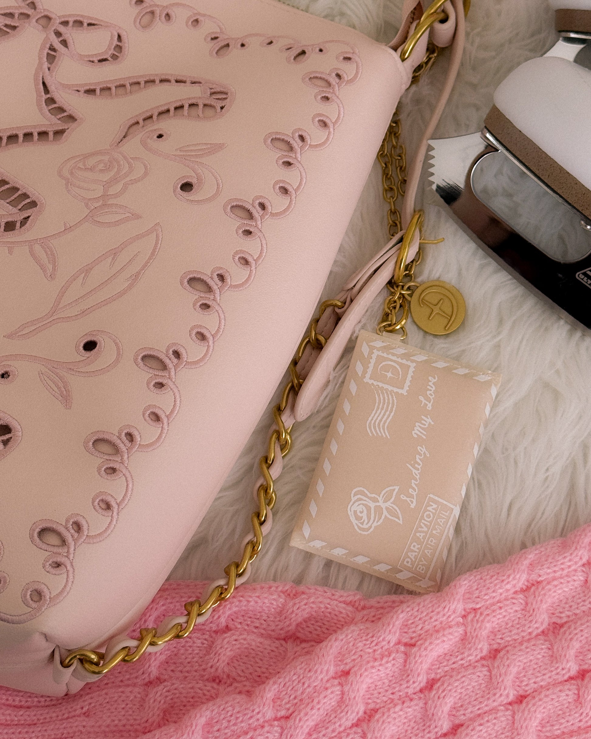 Pink handbag with gold chain and decorative tag on a textured surface